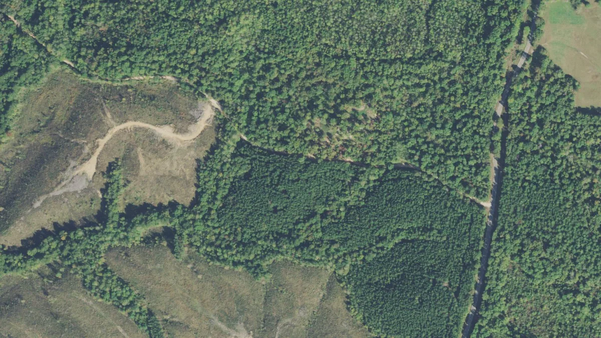 Aerial photograph of wooded ridge country with a road along one edge.
