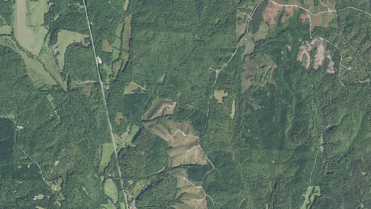 Wider aerial photograph showing the road network and surrounding woodland.