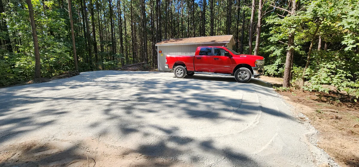 Gravel pad with a building and a parked pickup truck surrounded by pines.