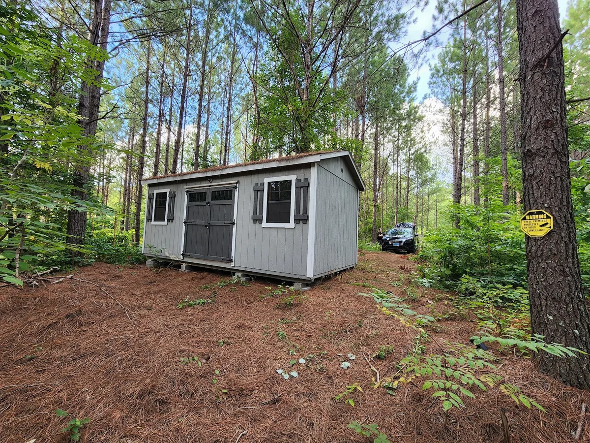 Grey wood building with white trim and double doors among the pines.