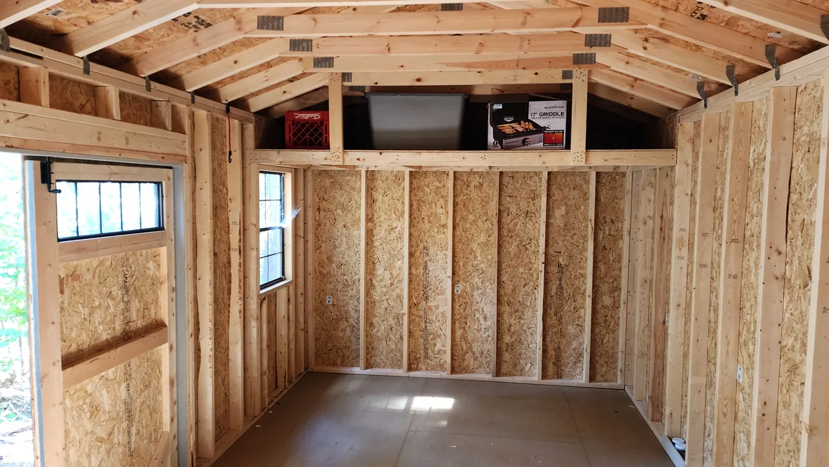 Interior of a wood building showing clean framing, a loft shelf and a window.